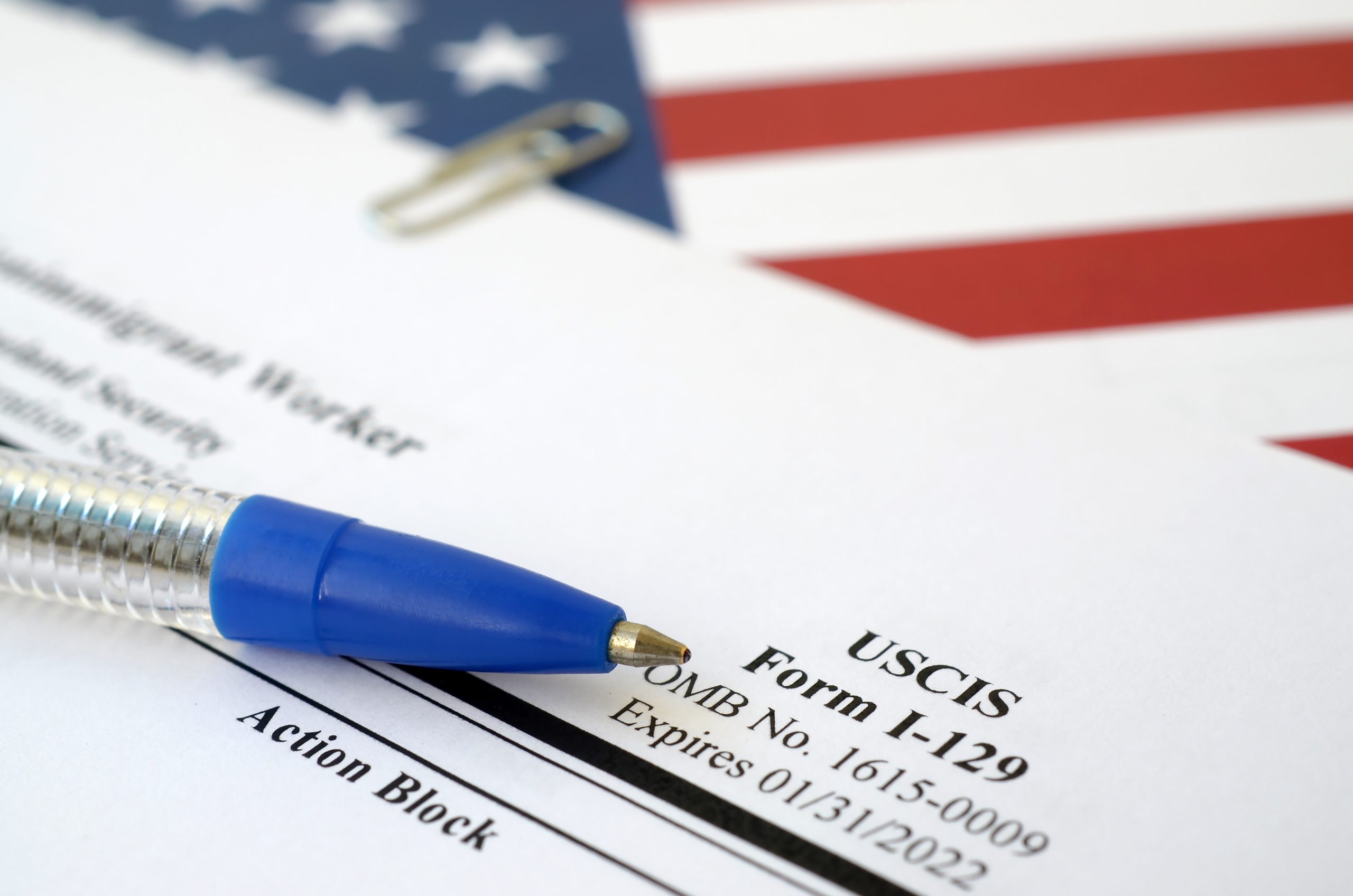 I-129 Petition for a nonimmigrant worker blank form lies on United States flag with blue pen from Department of Homeland Security